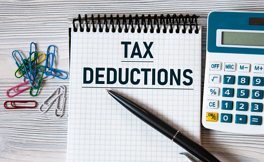 TAX DEDUCTIONS - words on a notebook on a light wooden background with a calculator and a pen. Business concept