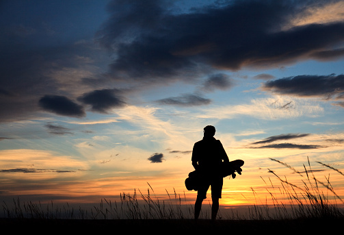 Back view of a male golfer in silhouette on a vast, windswept links course. Male golfer is a senior and is unrecognizable. Classic golf atmosphere with fescue grass, beautiful sky, and golfer walking and carrying his golf bag.