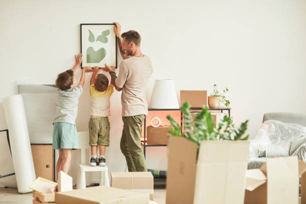 Hanging Picture Together Full length portrait of happy father with two sons hanging pictures on wall while moving in to new home, copy space hanging stock pictures, royalty-free photos & images