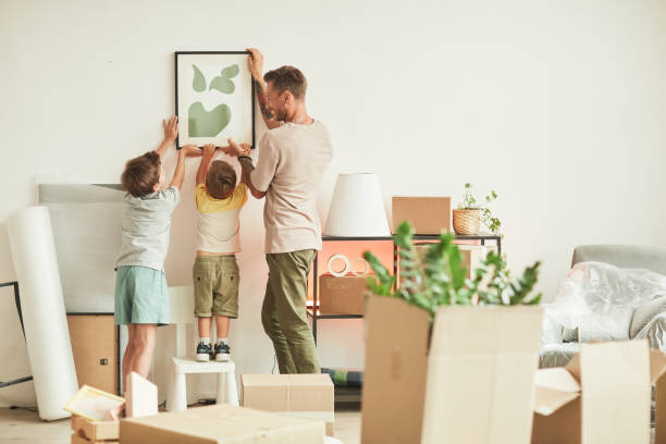 Hanging Picture Together Full length portrait of happy father with two sons hanging pictures on wall while moving in to new home, copy space relocation stock pictures, royalty-free photos & images