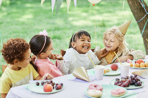 Portrait of smiling little girl with friends at picnic table outdoors enjoying Birthday party in Summer