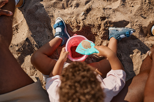 Top view portrait of young African-American father and son playing in sand together at beach, copy space