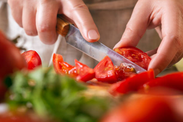 istock Chef slicing tomato using knife on the table in restaurant. Process of cutting and preparation food in kitchen. 1349053042