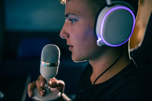 teenage boy talking into a microphone in a dark room, wearing headphones
