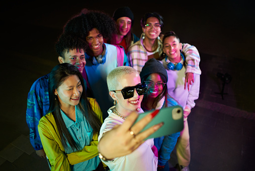 Group of friends taking selfie with mobile phone having fun at the party at night. Crowd of happy multiethnic people. High quality photo