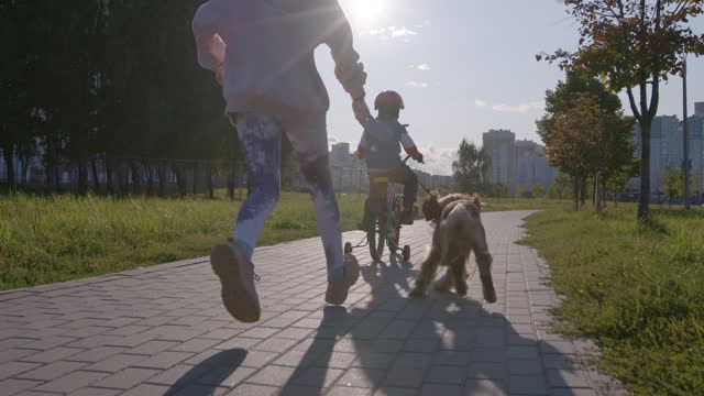 The older sister runs with the dog after the younger brother riding a bike.