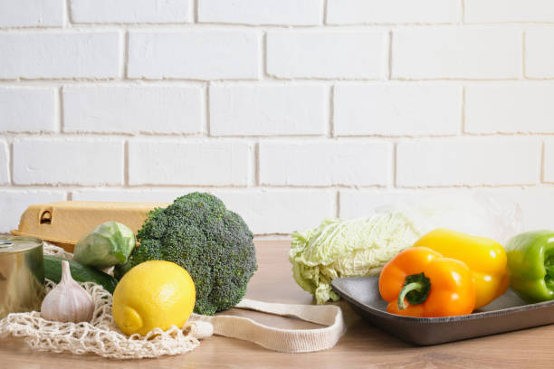istock vegetables in a mesh shopping bag and plastic wrapped on a rustic kitchen table, say no to alstik, using reusable shoppers instead of plastic wraps 1349061966