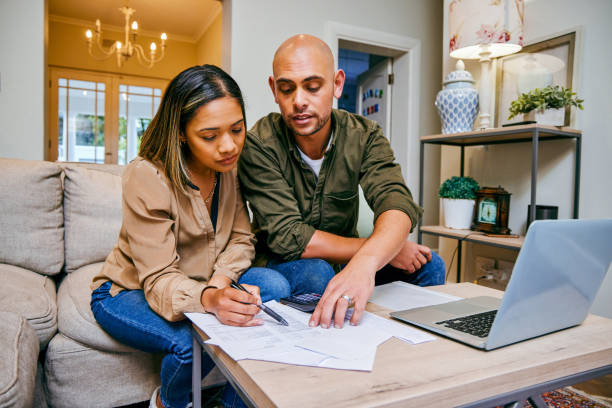 shot of a young couple reviewing their finances while using their laptop - paper document notebook laptop imagens e fotografias de stock