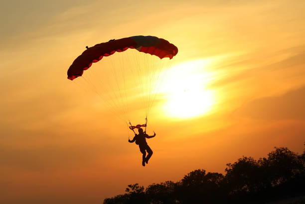 skoczek spadochronowy lądujący na spadochronie o zachodzie słońca - parachute zdjęcia i obrazy z banku zdjęć