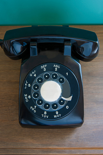 Old black telephone on wooden desk.