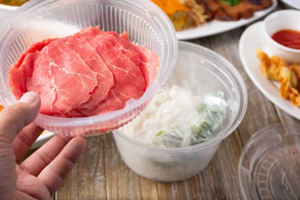 A view of a hand holding a compartment to a to-go plastic container designed for pho ingredients.