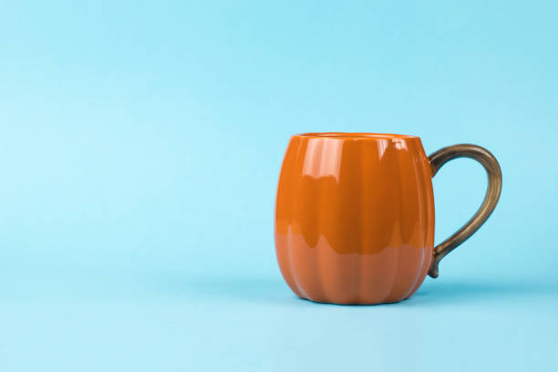 istock A bright orange pumpkin-shaped coffee mug on a blue background. 1349087847