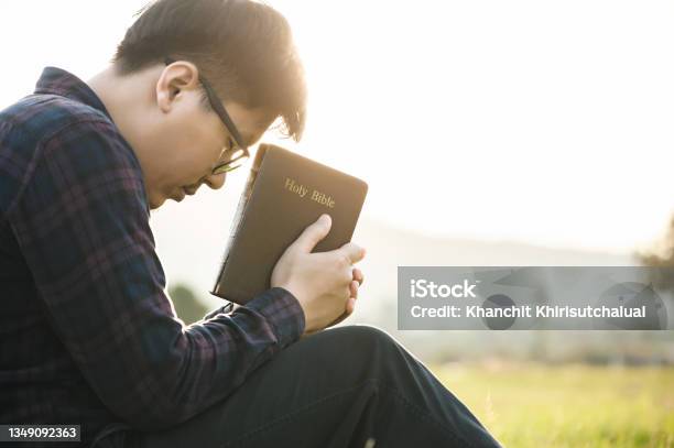 Christian Man Sit Holds The Bible In Hands To Reading The Holy Bible And Pray In A Field During A Beautiful Sunset The Concept For Faith Spirituality And Religion Peace Hopesit Stock Photo - Download Image Now