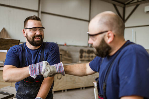 Happy male carpenters fist bumping in a workshop. Happy male carpenters talking while fist bumping in a workshop. blue collar worker stock pictures, royalty-free photos & images
