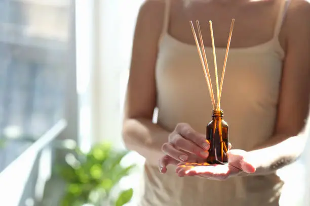 Woman holding diffuser with wooden sticks for aroma oil, close-up. Aromatherapy at home, fragrance perfume