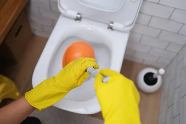 Hands in yellow gloves hold a plunger at the toilet, close-up. Removing a blockage in plumbing