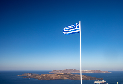 Greek Flag over Nea Kameni Island on Santorini in The Cyclades, Greece. A cruise ship is visible.