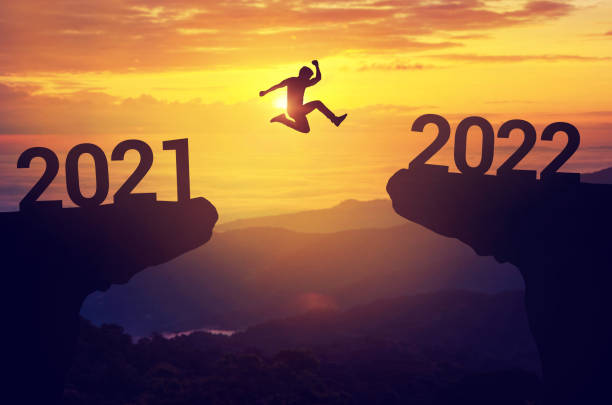 силуэт человека прыгает между 2022 и 2022 годами с закатным фоном, успех новогодней концепции. - happy new years стоковые фото и изображения