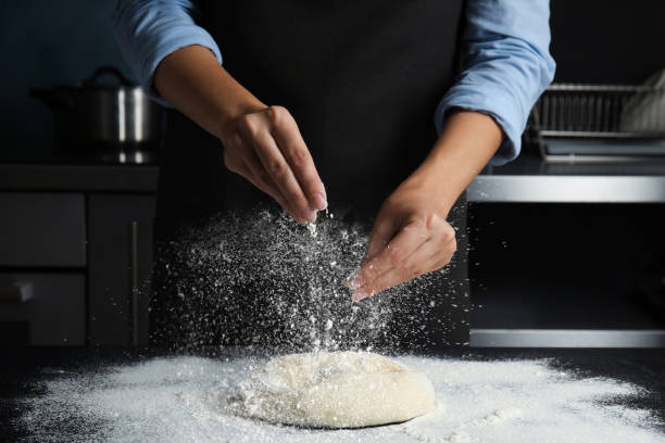 istock Woman sprinkling flour over dough on table in kitchen, closeup 1349121144
