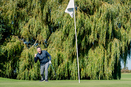 Golfer celebrating as he ball drops in to the hole. Colour, horizontal format with lots of copy space, photographed on location at a golf course on the island of Moen in Denmark.