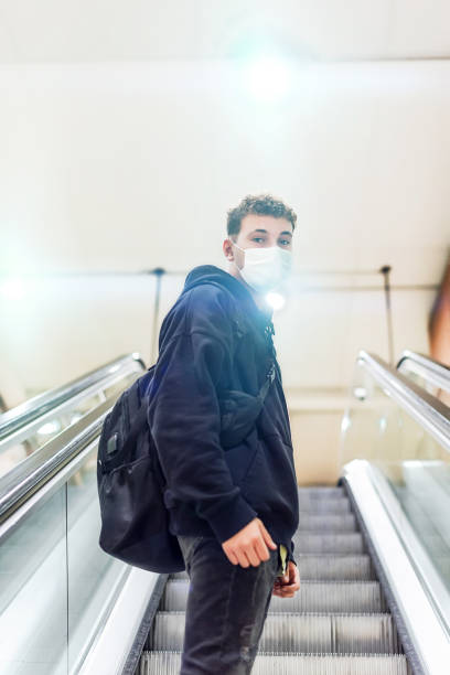 istock Young man with a backpack and white mask climbing an escalator in a metro station 1349128490