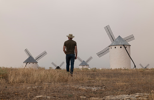 A man wearing a cowboy hat with windmills in the countryside