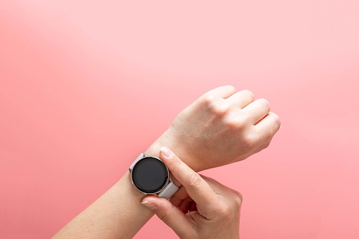 Modern watch on womans hand on pink background. Time concept, top view template