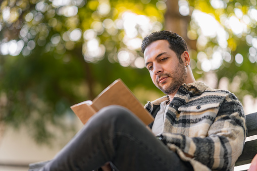 A handsome man is relaxing and reading a book in nature.