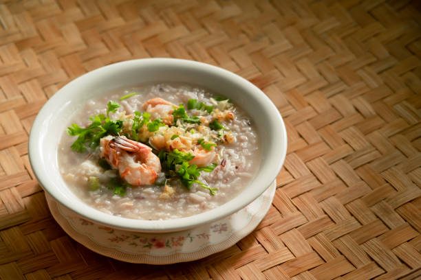 gekochte reisklarsuppe mit garnelen und grünem blattgemüse in einer weißen keramikschüssel auf dem bambuswebhintergrund. einfaches frühstück essen hausgemachtes konzept. top-ansicht food stylist menü mit kopierraum - oatmeal porridge heat cereal stock-fotos und bilder