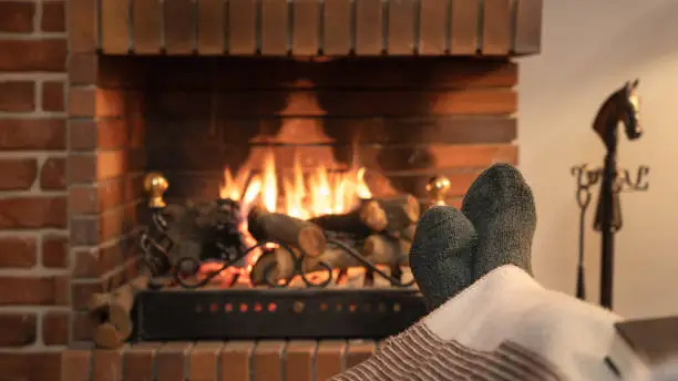 Photo of Feet in socks in front of the fire of a fireplace in winter.