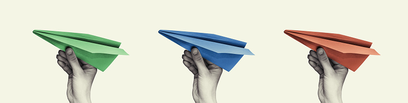 Three paper airplanes of different colors in a woman hands. Isolated background.