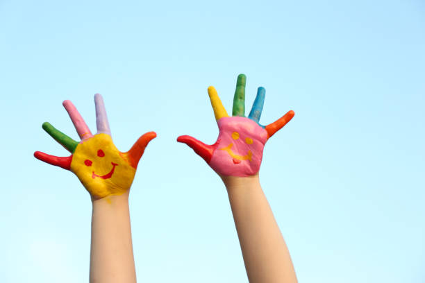 istock Kid with smiling face drawn on palms against blue sky, closeup. School holidays 1349143361