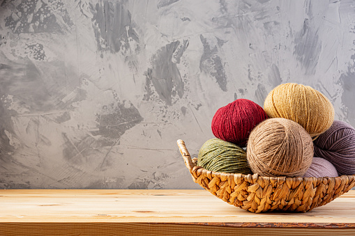 Skeins of yarn for knitting from natural wool in a wicker basket. Wooden surface or table. Background - concrete wall.