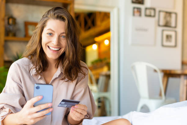 Woman sitting in bed makes an order through a mobile application. She dials the card number for online purchases stock photo