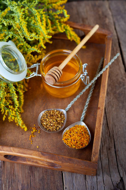 Bee pollen granules. Fresh honey on wooden table. Still life bee product background. Wooden spoon with small glass jar closeup. Eco food. Selective focus, copy space stock photo