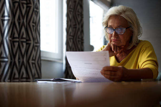 istock Senior woman with eyeglasses on is sitting at the table, reading reports. 1349147406