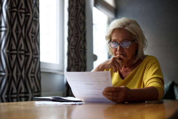 Worried senior lady is sitting at the table, reading report.
