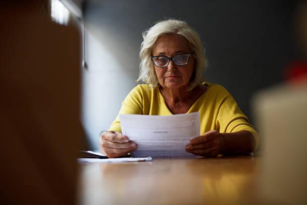 istock Selective focus. Senior woman with eyeglasses on is sitting at the table, focused on paperwork. 1349148595