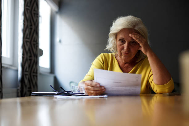 istock Senior woman is sitting at the table, holding her forehead and reading reports. 1349148624