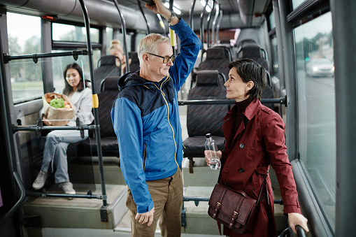 Side view portrait of two adult people chatting while standing in bus and traveling by public transport in city, copy space