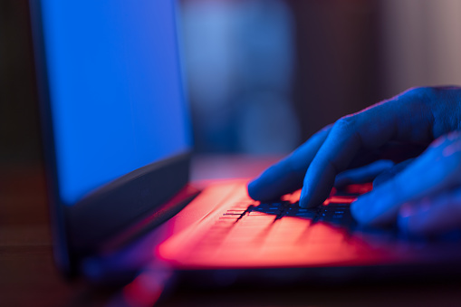 Man using laptop in the dark with blue glow of screen. This file is cleaned and retouched.