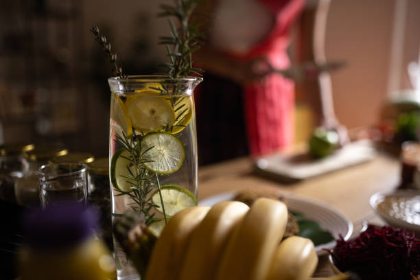 Infused water detox drink in bottle on table, woman preparing healthy meal in background