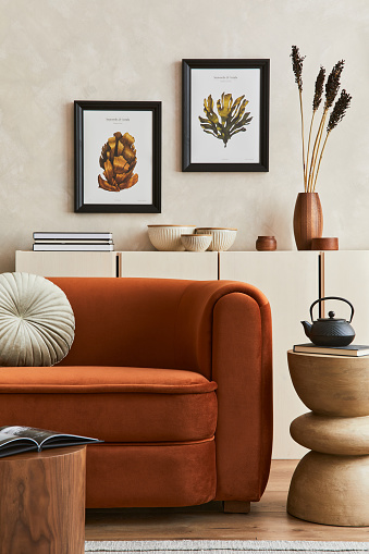 Creative composition of stylish living room interior with two mock up poster frames, orange sofa, beige commode, coffee table and stylish personal accessories. Artistic space. Template.