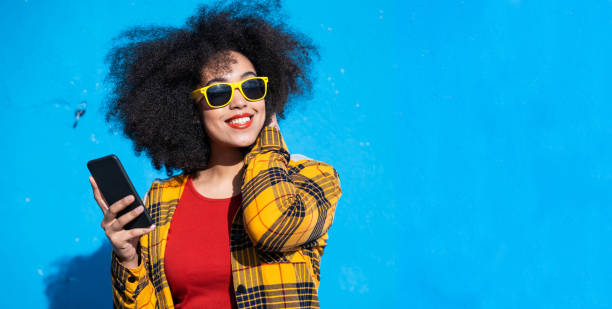 istock Smiling american-african woman using smart phone on a blue background 1349164165