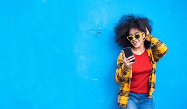 istock Smiling american-african woman using smart phone on a blue background 1349164167