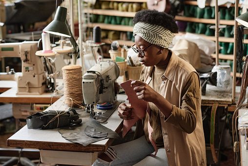 African seamstress sewing two pieces of fabric together on sewing machine at her workplace in the workshop