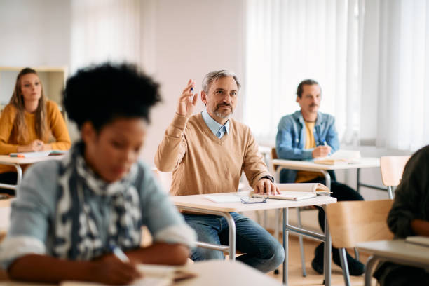 mature student raising his hand to ask a question during a class at lecture hall. - night school imagens e fotografias de stock