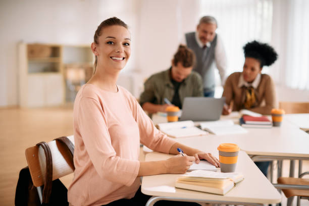 istock Happy woman writing notes while studying in the classroom and looking at camera. 1349168653