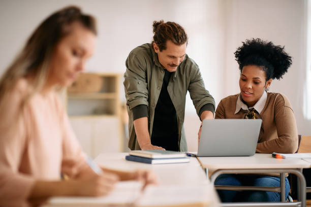 istock Happy mid adult students cooperating while using laptop in the classroom. 1349168806