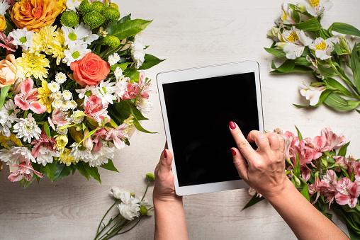 smartphone in hand against the background of a bouquet of flowers. order flowers and their delivery. bouquet of flowers on a light wooden background with space for text